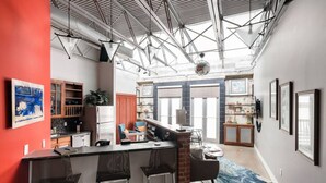 A modern kitchen with a bar area, large windows, and a high ceiling with exposed beams. - Green Door Lofts-Retro Loft - Silos/Downtown (Waco)