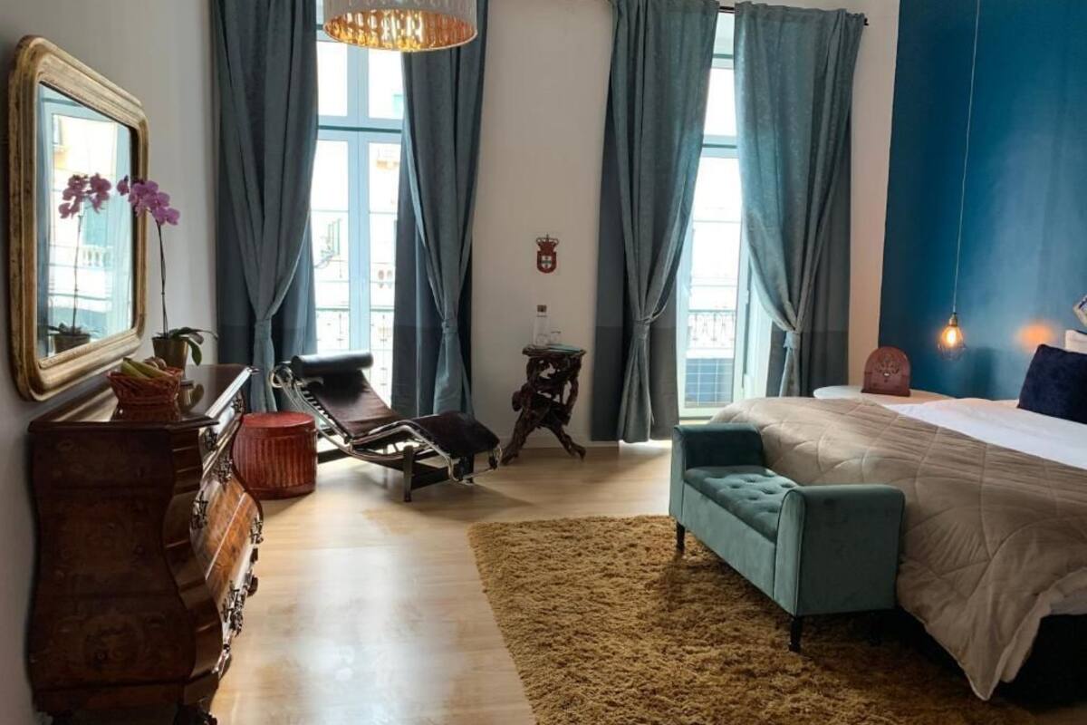 Un dormitorio con cama, cómoda, silla, alfombra y ventana con cortinas.
