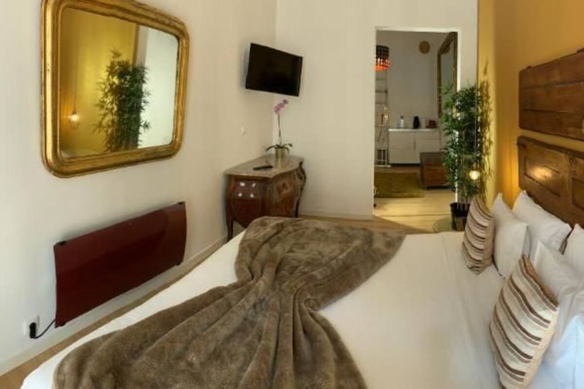 Una habitación de hotel con cabecera de madera, un espejo grande, un televisor de pantalla plana y una cama con una manta marrón.