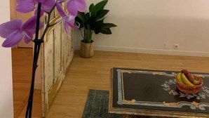 Ein Zimmer mit einem an der Wand befestigten Fernseher, einem Tisch mit Obstkorb und einer Topfpflanze.