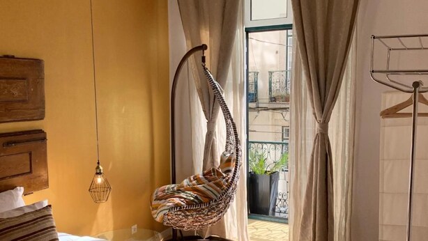 Ein Schlafzimmer mit einer Hängematte, einem Bett mit Kissenstreifen und einer Hängeleuchte, mit Blick auf den Balkon.