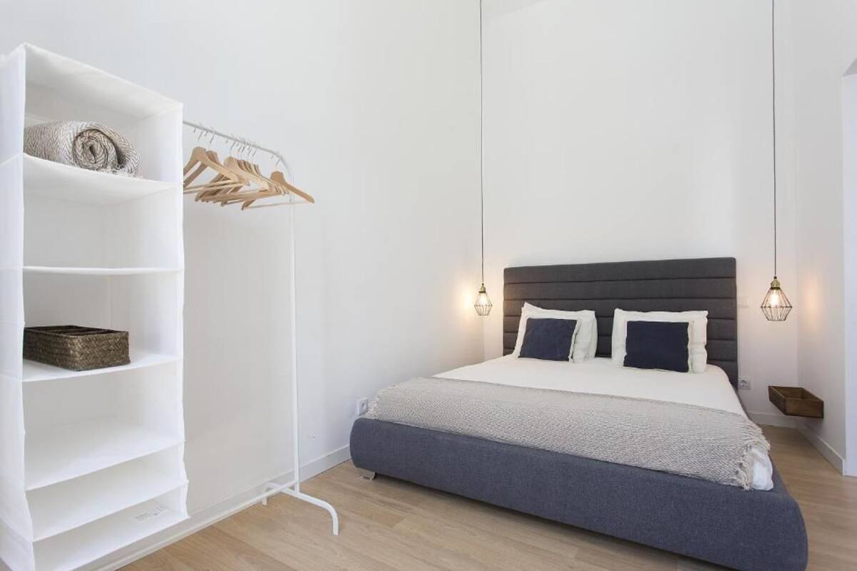 Un dormitorio con cama, estantería blanca y un perchero de madera.