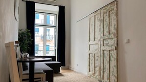 Ein Zimmer mit Esstisch, Stühlen, einer Zimmerpflanze und einem großen Fenster mit Vorhängen.