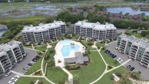 A multi-story hotel with a central swimming pool, surrounded by lush greenery and a lake. - Litchfield Beach 3Bed/3Bath w Sleeper sofa Oceanfront Condo in Pawleys Island SC (Pawleys Island)