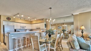 A spacious kitchen with white cabinets, a central island, and a dining area with a glass table and chairs. - Litchfield Beach 3Bed/3Bath w Sleeper sofa Oceanfront Condo in Pawleys Island SC (Pawleys Island)