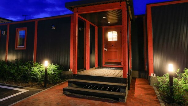 A building with a red entrance, a wooden porch, and a brick pathway leading to the door. - Phottage inn Biei (Biei)