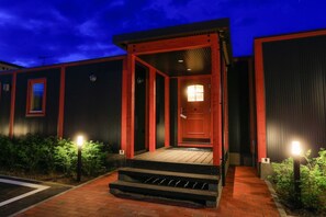 A building with a red entrance, a wooden porch, and a brick pathway leading to the door. - Phottage inn Biei (Biei)