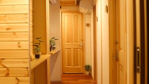 A wooden hallway with a wooden door at the end, a potted plant on the left, and a shelf with a plant on the right. - Phottage inn Biei (Biei)