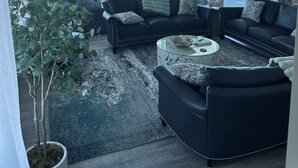 Ein Wohnzimmer mit großem Fenster mit Blick auf einen Strand, einem Deckenventilator und einer Topfpflanze.