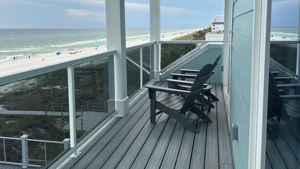 Eine überdachte Terrasse mit Blick auf den Strand, Holzmöbel und einem Geländer.