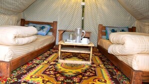 A cozy, triangular tent-style room with two beds, a small wooden table with a kettle and mug, and a colorful patterned carpet.