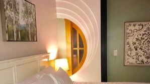 A bedroom with a bed, a nightstand, a lamp, and a wall with a circular design and a framed picture. - Green Door Lofts -Magnolia Loft, Silos/Downtown (Waco)