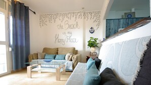 Un soggiorno con un divano, un tavolino in vetro e una parete con una frase decorativa.