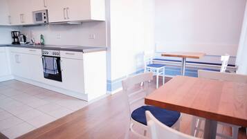 A modern kitchen with white cabinets, a microwave, a coffee maker, and a stove. There is a dining area with a wooden table and white chairs.