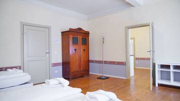 Quarto de hotel com soalho de madeira, guarda-roupa, candeeiro de pé e cama com roupa de cama branca.