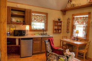 Una cocina acogedora con armarios de madera, microondas, lavamanos y una zona de comedor con una silla y mesa.