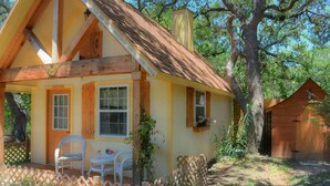A small, single-story house with a sloped roof, a porch with white chairs, and a wooden fence. - Rumpelstilzchen Cottage (#2) (Fredericksburg)