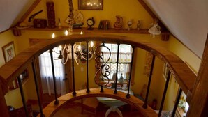 A wooden staircase with a wrought iron railing leading to a second-floor area with various decorative items and a window with curtains. - Rumpelstilzchen Cottage (#2) (Fredericksburg)