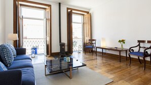 Una sala de estar con un sofá, una mesa de centro, una silla, una mesita con una lámpara y un ventanal con vistas a un balcón.
