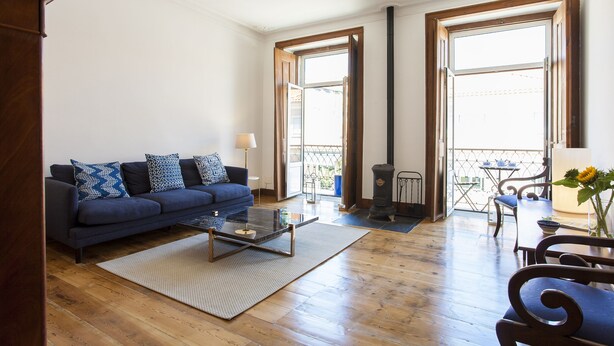 Un salón con un sofá azul, una mesa de centro de vidrio y piso de madera.