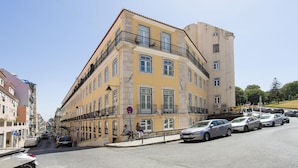 Un edificio de varios pisos con balcones, una calle al frente y automóviles estacionados.