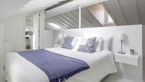 Un dormitorio moderno con una cama grande, paredes blancas y un tragaluz.