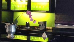 En receptionsdisk med en skærm med grønt lys, en lilla orchidé og en kaffemaskine.