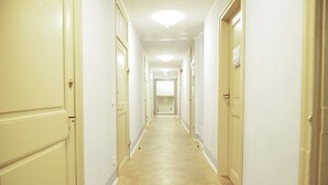 Corredor longo e estreito de hotel, com portas cor creme e piso de madeira clara.