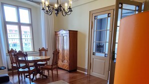 Un salon comprenant un coin repas, des meubles en bois, un lustre et une vue sur l’extérieur grâce à de grandes fenêtres.