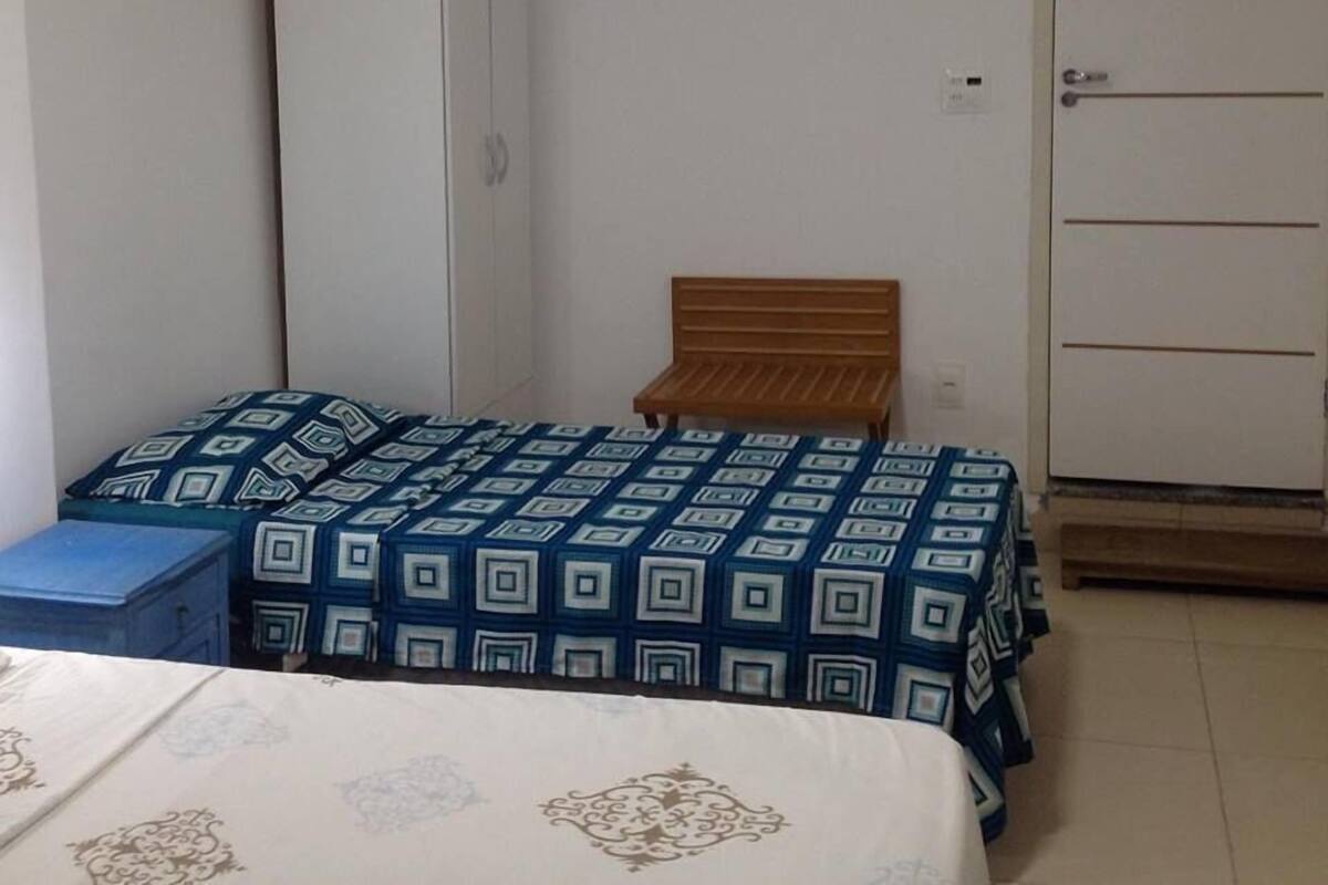 Un dormitorio pequeño y sencillo con una cama individual, un banco de madera, un armario y una puerta.
