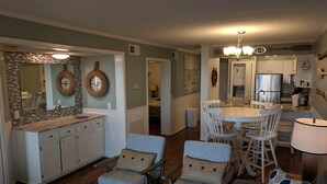 Eine moderne Küche mit weißen Schränken, ein Essbereich mit einem runden Tisch und Stühlen sowie ein Wohnzimmer mit einer Couch und Sesseln.