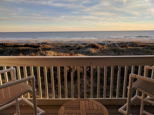 Eine Holzterrasse mit zwei Korbstühlen, die auf den Strand ausgerichtet sind.