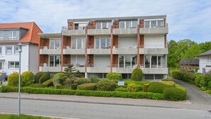 En flervåningsbyggnad med bostäder, balkonger, en asfalterad uppfart och välskött trädgård.