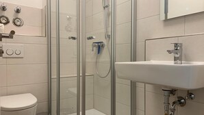 Ett modernt badrum med en dusch som är avskärmad med glasväggar, ett vitt handfat och en toalett.