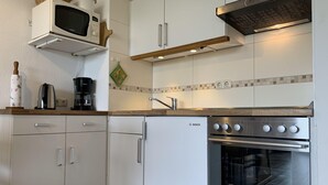 Ett modernt kök med vita skåp, ett kylskåp från Bosch, en mikrovågsugn, en kaffebryggare och en spis.