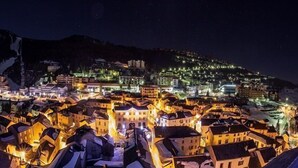 A town at night with buildings illuminated, a snow-covered hill in the background, and a river or lake in the foreground.