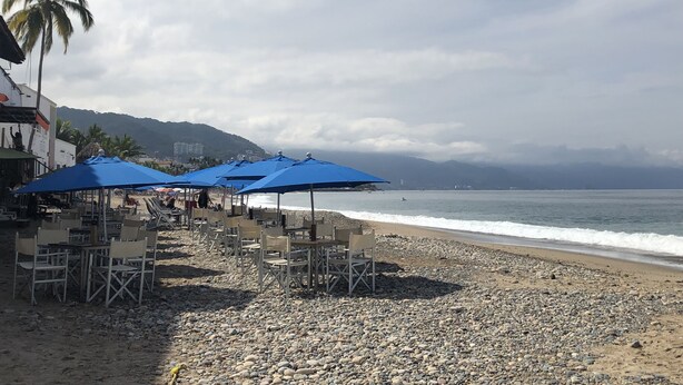 Un café situé en bord de mer, avec une terrasse et des parasols, offrant une vue sur l’océan.
