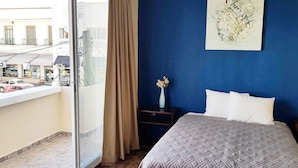 Une chambre d’hôtel avec un lit, une table de chevet, un vase de fleurs et une vue sur la rue.