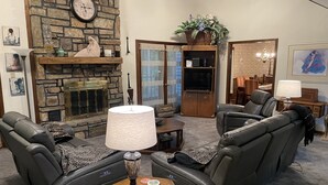 A living room with leather sofas, a stone fireplace, a television, and a dining area with a chandelier.