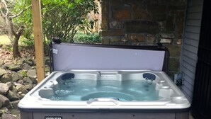 A Viking Spa hot tub with a step for access, set outdoors with a stone wall and greenery in the background.