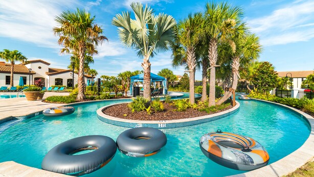 A swimming pool with three inflatable rings, palm trees, and a gazebo. - Spacious Villa for Large Groups ✦ Lazy River and Tiki Hut ✦ (Kissimmee)