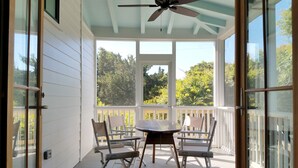 Un portico coperto con una ventola a soffitto, ringhiere bianche e un tavolo con sedie.