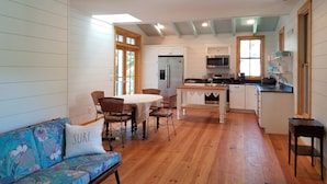 Cucina spaziosa con pavimento in legno, mobili bianchi, isola centrale e zona pranzo con sedie in vimini.