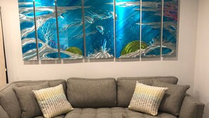 A modern living room with a sectional sofa, a coffee table, and a large ocean-themed painting on the wall.