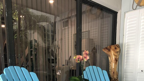 Two light blue Adirondack chairs with a small table and a potted orchid between them.
