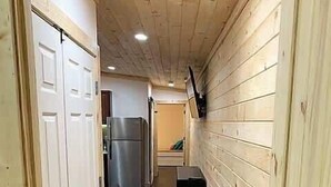 Un couloir étroit aux murs en bois et au plancher sombre, qui mène à un coin cuisine équipé d’un réfrigérateur et d’un évier.