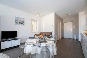 Un salon moderne avec une table à manger pour deux personnes, un canapé, un téléviseur à écran plat et un tableau accroché au mur.
