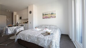 A modern bedroom with a large bed, a dining area, and a kitchen in the background. - Sunrise House with Balcony and Parking, Lugano, Switzerland (Lugano)