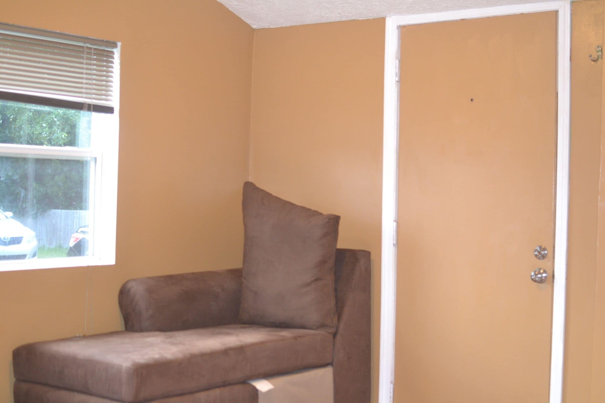 A room with a brown couch, a window with blinds, and a door with a handle.