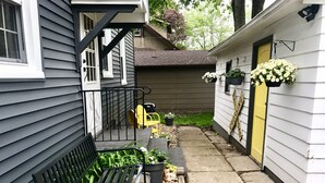 Un étroit sentier mène à une maison où se trouvent un banc et des plantes en pot.